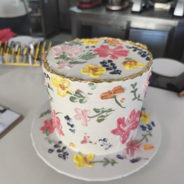 Bolo floral com flores pintadas à mão e borda dourada em buttercream.